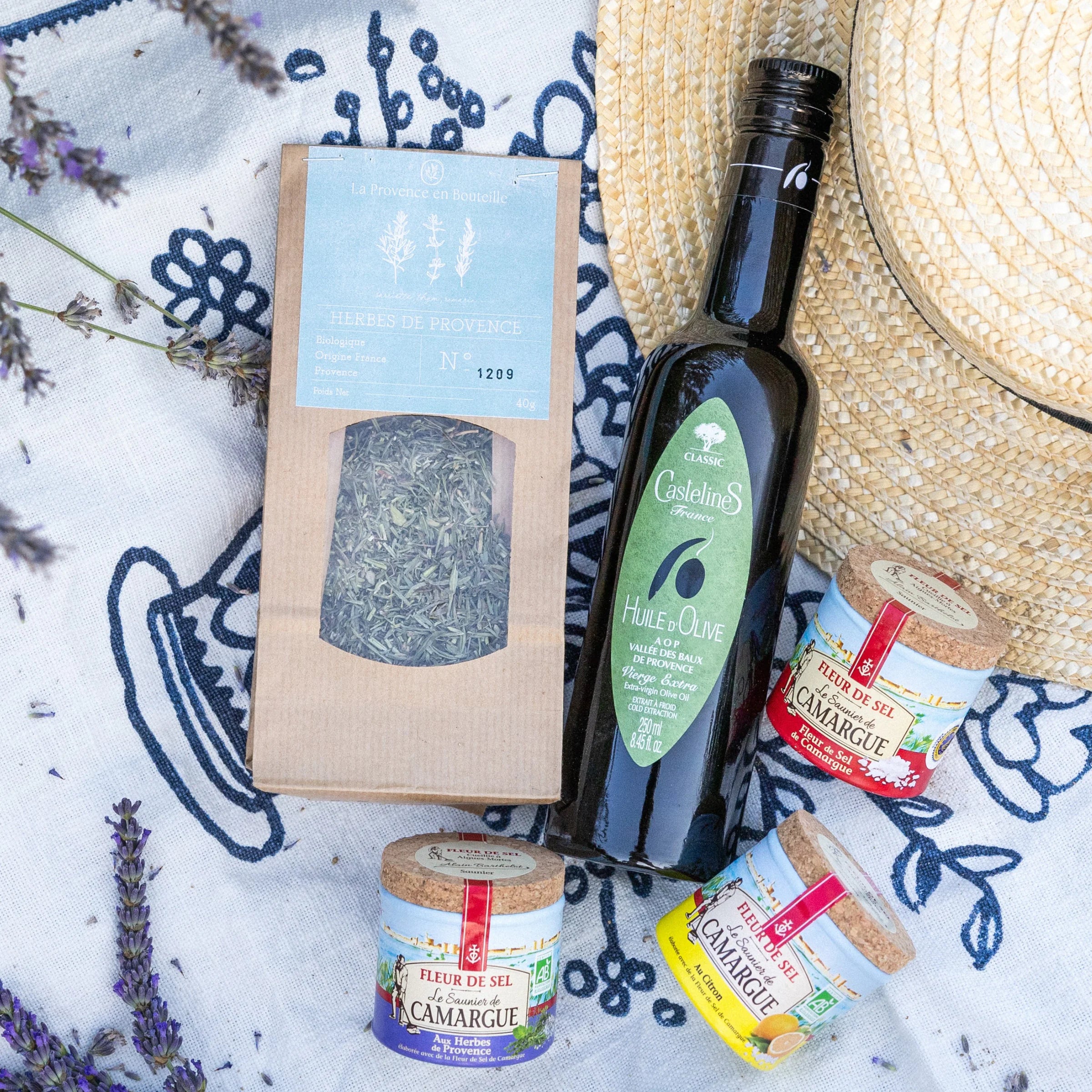 Condiment Essentials gift box with olive oil, Fleur de Sel trio, Provence herbs and salt spoon on Provençal tablecloth with straw hat