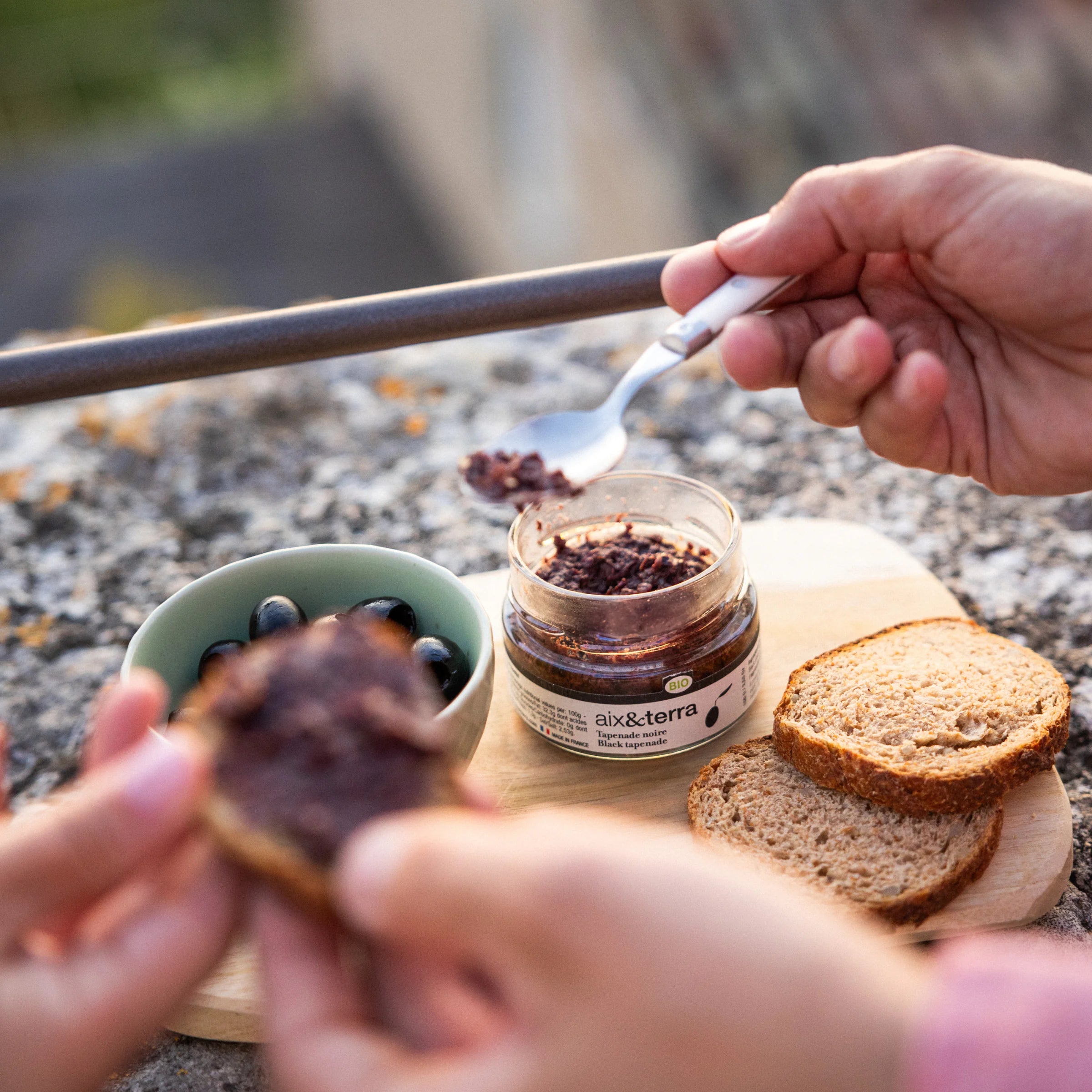 Spreading Aix&Terra organic black tapenade on bread with black olives, outdoor Provençal aperitif