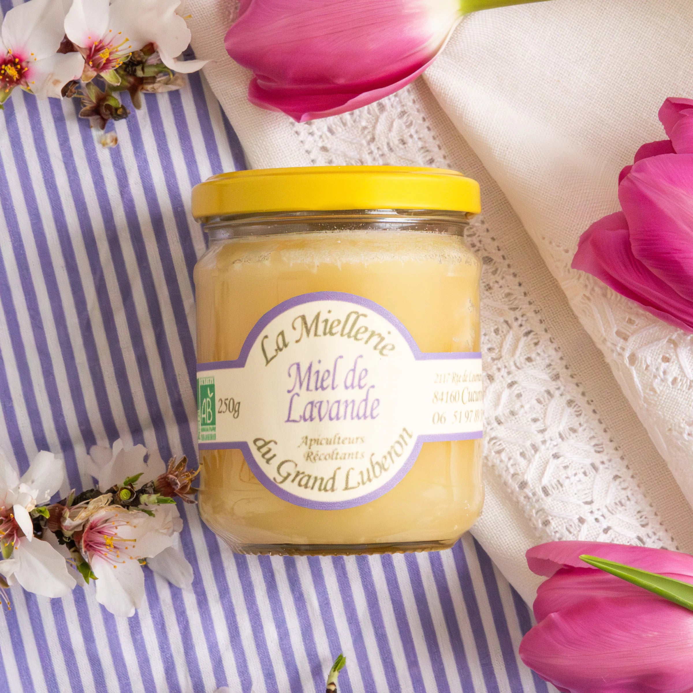 Spring Flavours gift box flat lay with almond croquants, organic lavender honey and Provence herbs on Provençal striped fabric with cherry blossom and tulips