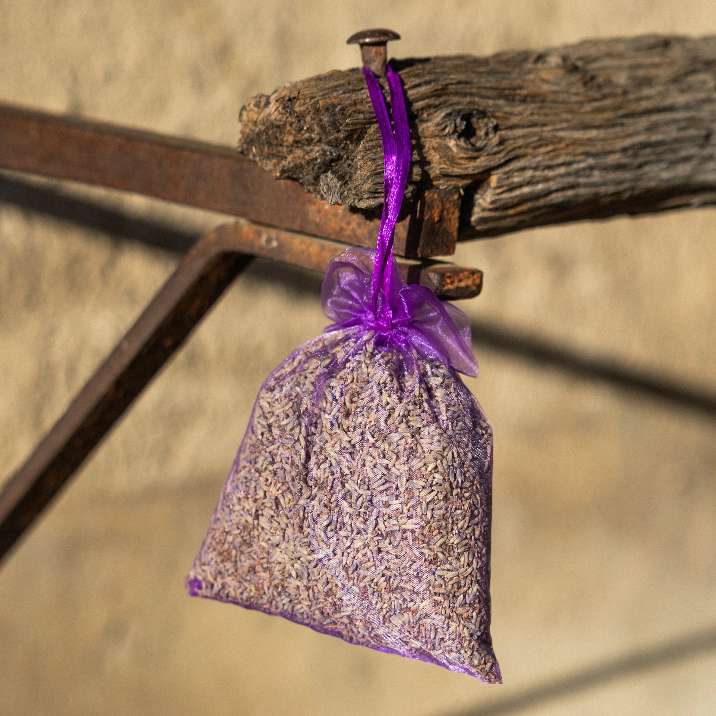 Organic dried lavender pouch hanging from a rustic iron frame with stone wall, Provence
