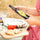 Female hands holding Castelines lemon and thyme olive oil over an outdoor Provençal lunch table with tomatoes, bread and tapenade