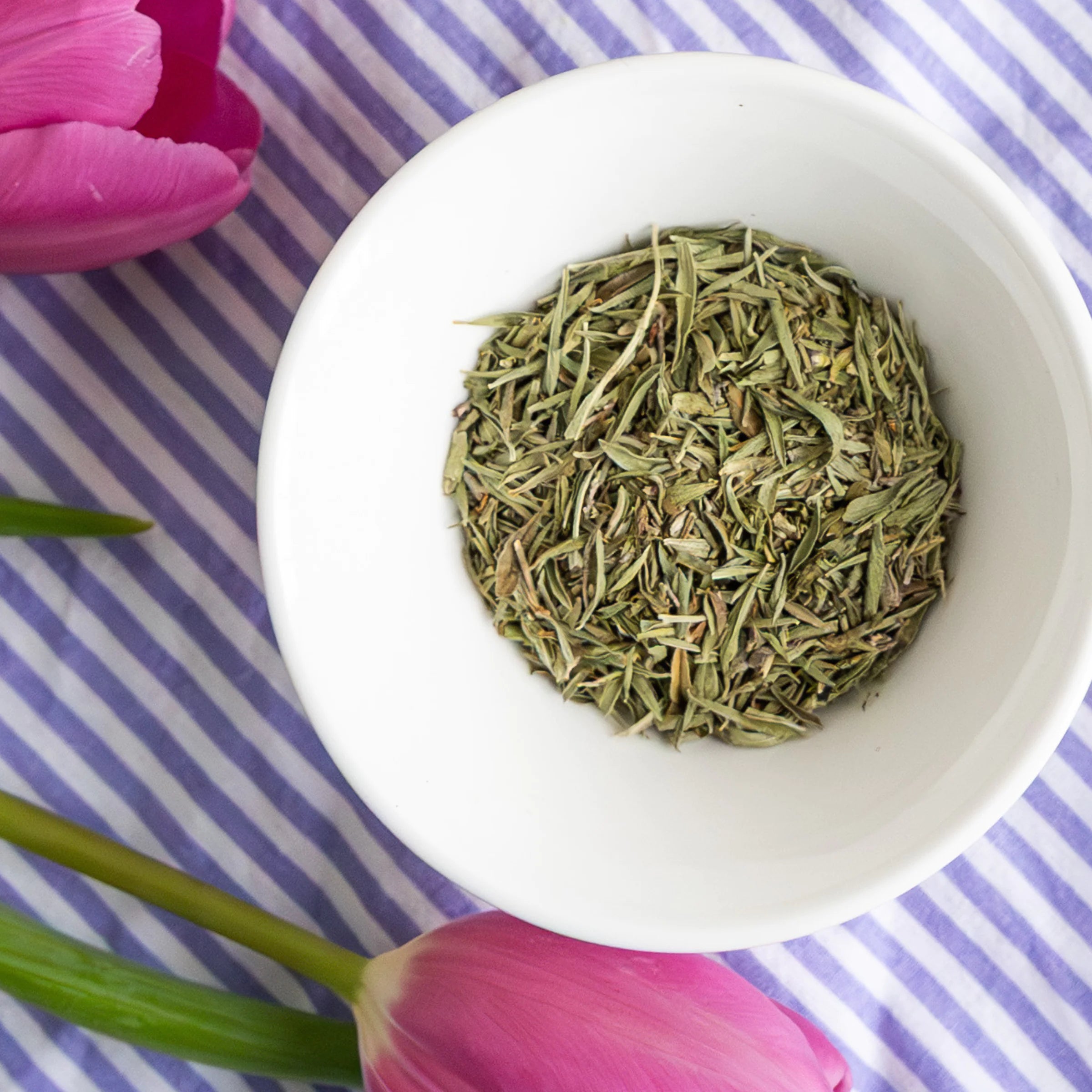 Overhead view of organic dried Provence herbs in a white bowl with pink tulips