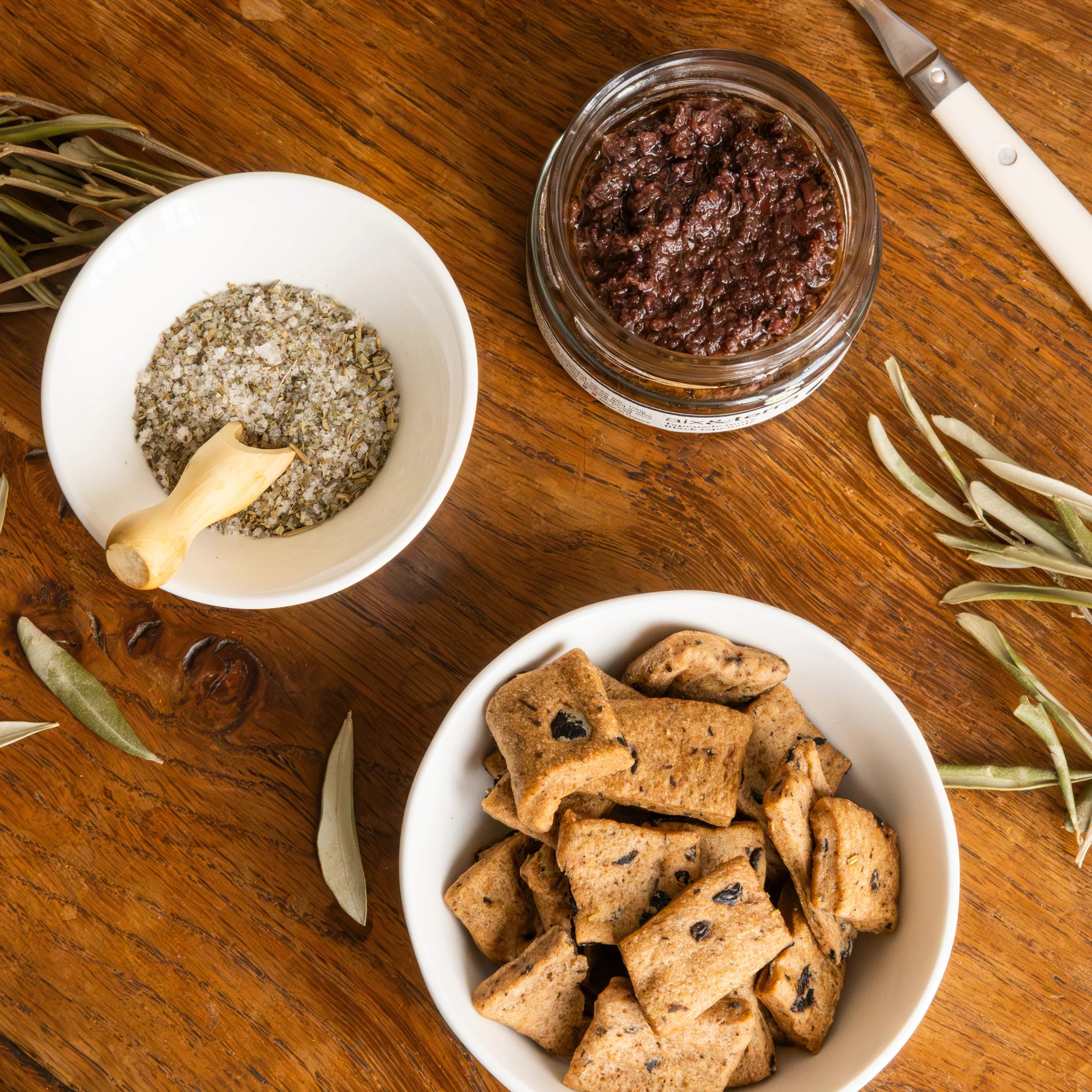 Flat lay of Provençal Apéro Father's Day gift box with open black tapenade, Fleur de Sel with herbs and olive biscuits with olive branches