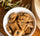 A white bowl filled with artisanal savory biscuits with black olives, placed on a rustic wooden table with olive branches, representing the authentic flavors of the Provençal pantry.