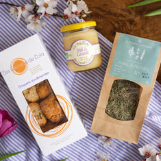 Spring Flavours gift box flat lay with almond croquants, organic lavender honey and Provence herbs on Provençal striped fabric with cherry blossom and tulips