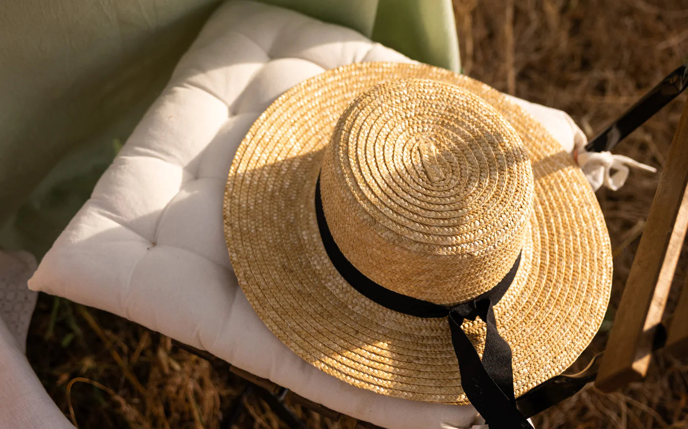 Wide-brimmed straw hat with black ribbon on a white cushioned chair, golden dry herbs, Provençal summer detail
