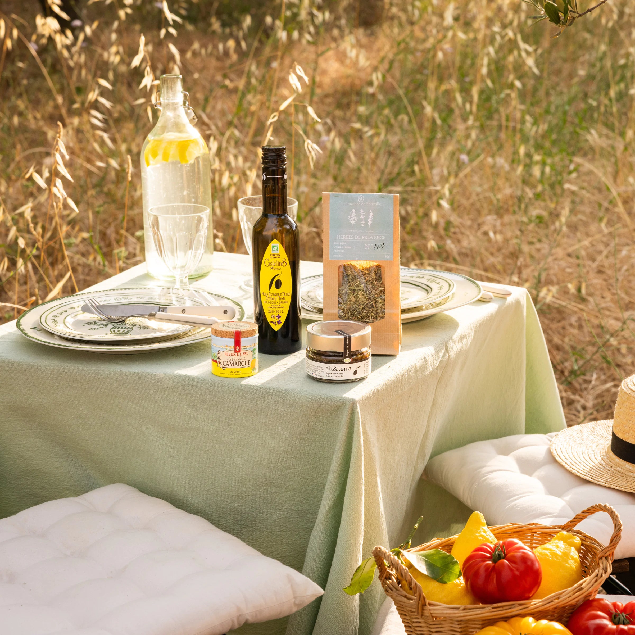 The Summer Table collection with lemon olive oil, Fleur de Sel, black tapenade and Provence herbs on an outdoor sage green table with seasonal vegetables, Provence
